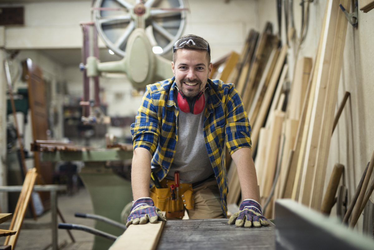 portrait-young-motivated-carpenter-standing-by-woodworking-machine-his-carpentry-workshopm Właściciel stolarni zadowolony faktoringu w BREWE